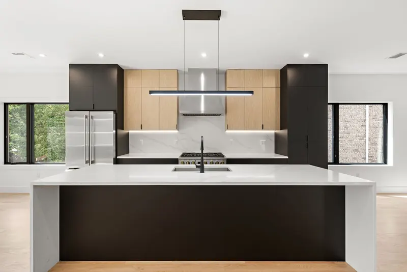 Modern black and oak kitchen in Cliffside Park, NJ: Flat-panel black and white oak cabinets, marble-look waterfall island