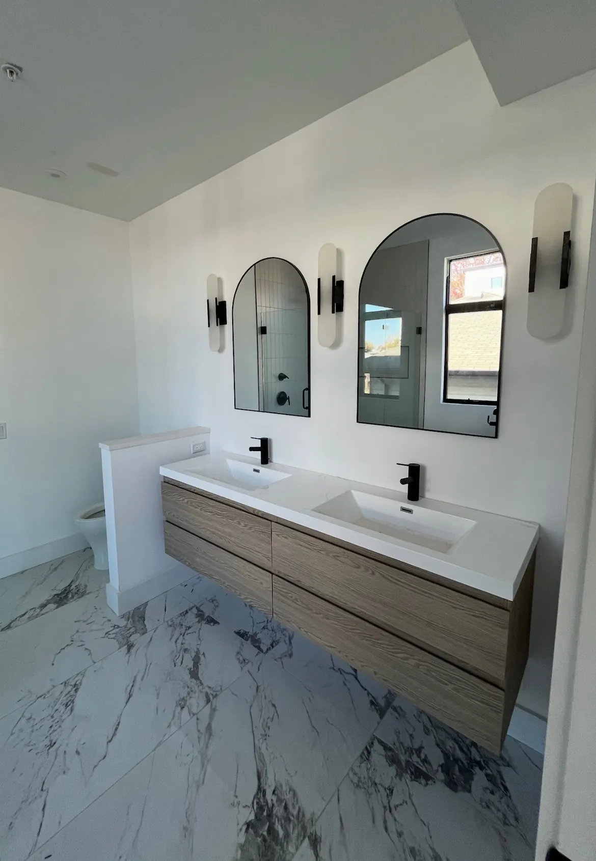Floating vanity with two arched mirrors and marble-look tile