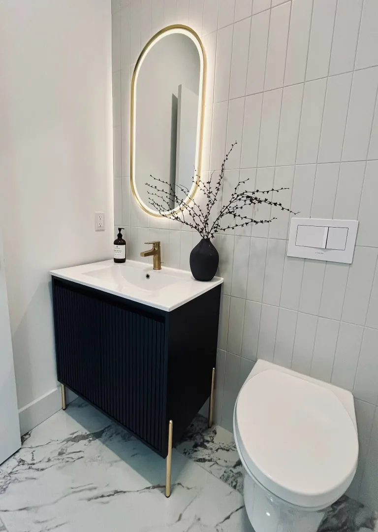 Fluted vanity powder room in Tenafly, NJ: Fluted navy vanity on brushed gold legs, white vertical wall tile, marble-look porcelain floor