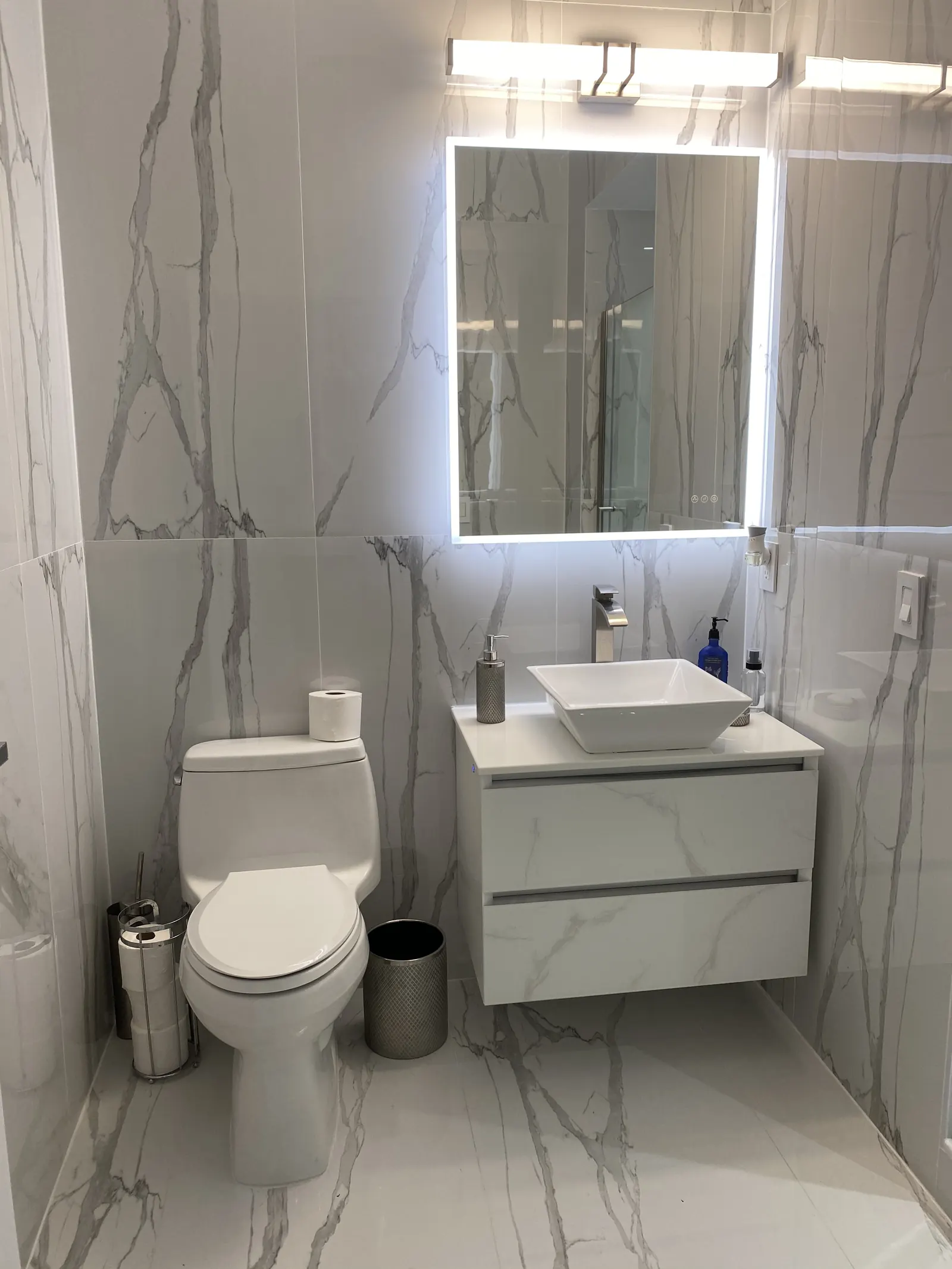 Gray floating vanity with LED mirror and marble-look wall tile