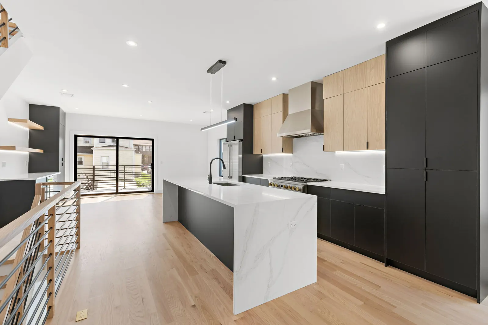 Open modern kitchen with black tall cabinets, oak uppers and waterfall island