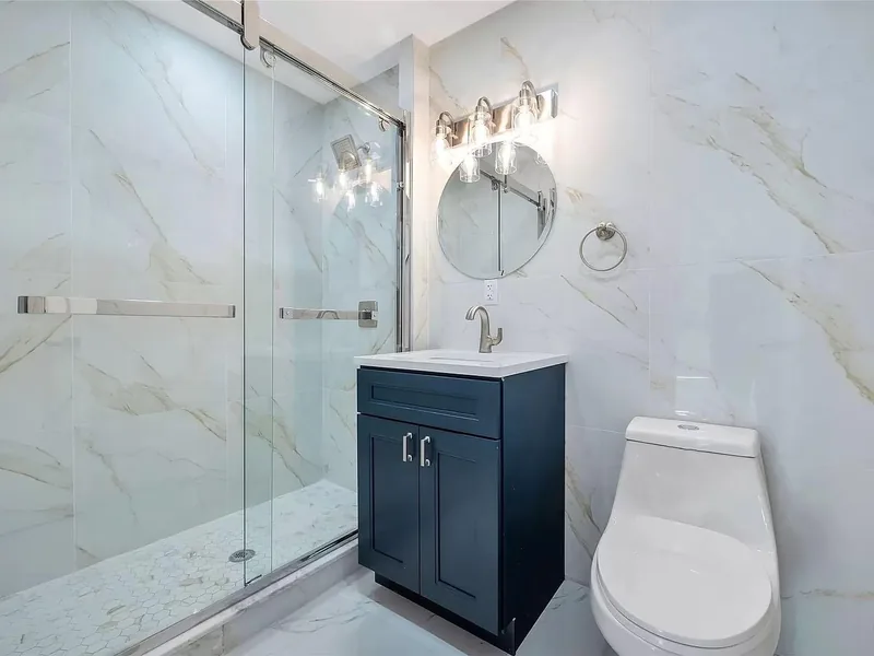 Navy shaker vanity bath in North Bergen, NJ: Gold-veined marble-look porcelain walls, navy shaker vanity, hexagon mosaic shower floor